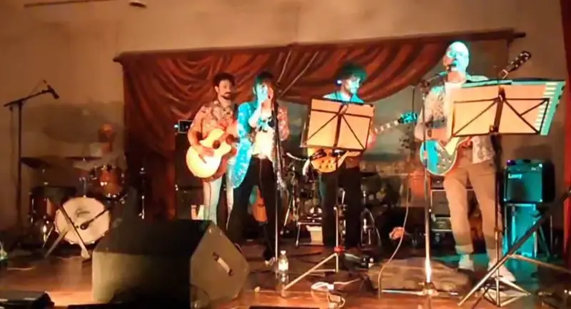 Le groupe sur scène dans une salle, devant un rideau rouge